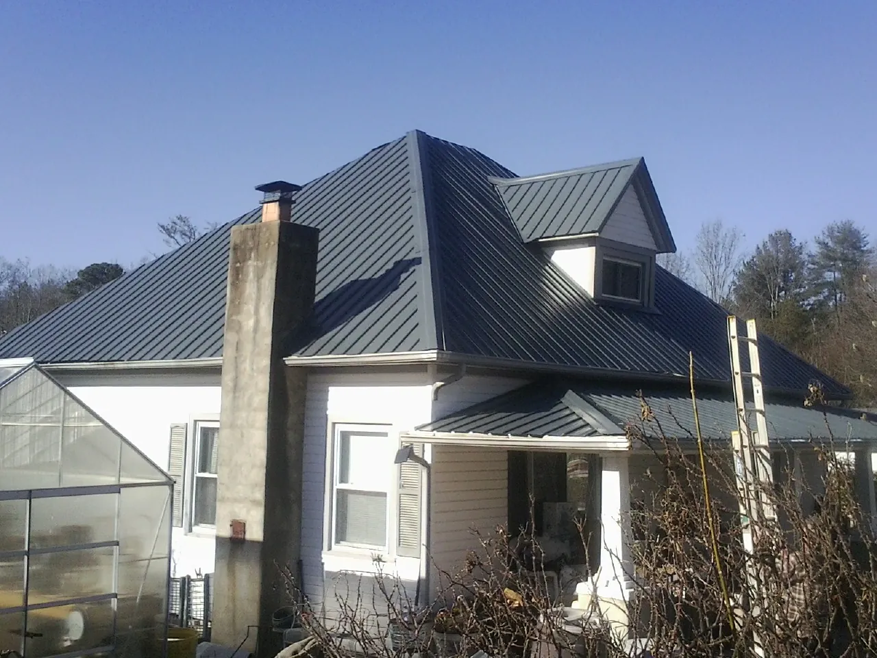 Dark blue standing seam metal roof on a white farmhouse with dormer — Slate & Tile Roof Repair by Roofing Brothers in Ottumwa