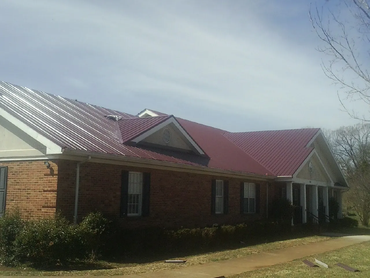 Red metal roof with gabled entries on a long brick building, from a Hail Damage Roof Repair job in Ottumwa