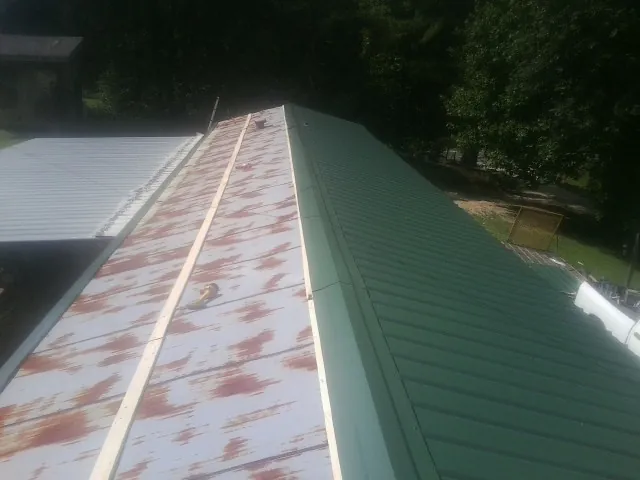 Old rusted panels beside newly installed green metal roofing — Wind Damage Roof Repair by Roofing Brothers in Ottumwa