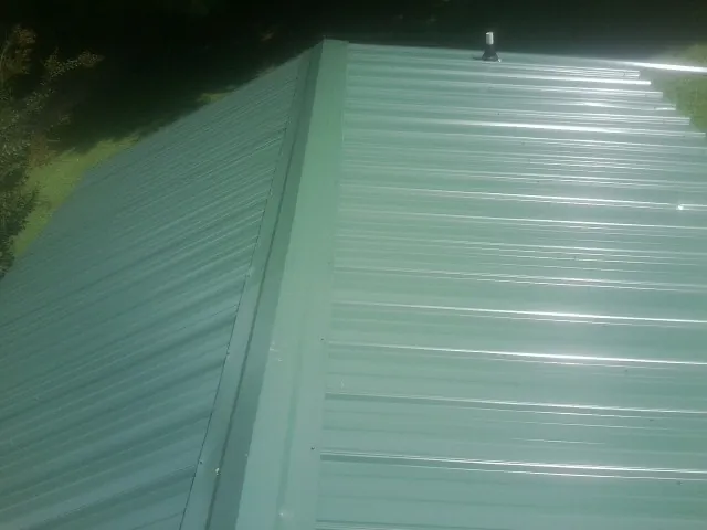 New green metal panels meeting at the ridge of a roof — Flat Roof Repair work by our crew in Ottumwa