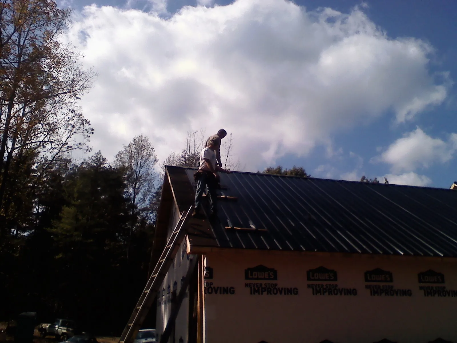 Roofer fastening dark metal panels high against a cloudy sky, from a Roof Inspection job in Ottumwa