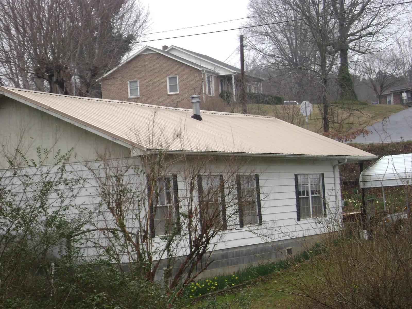 Tan metal roof on a white sided house set into a hillside — Commercial Roofing by Roofing Brothers in Ottumwa