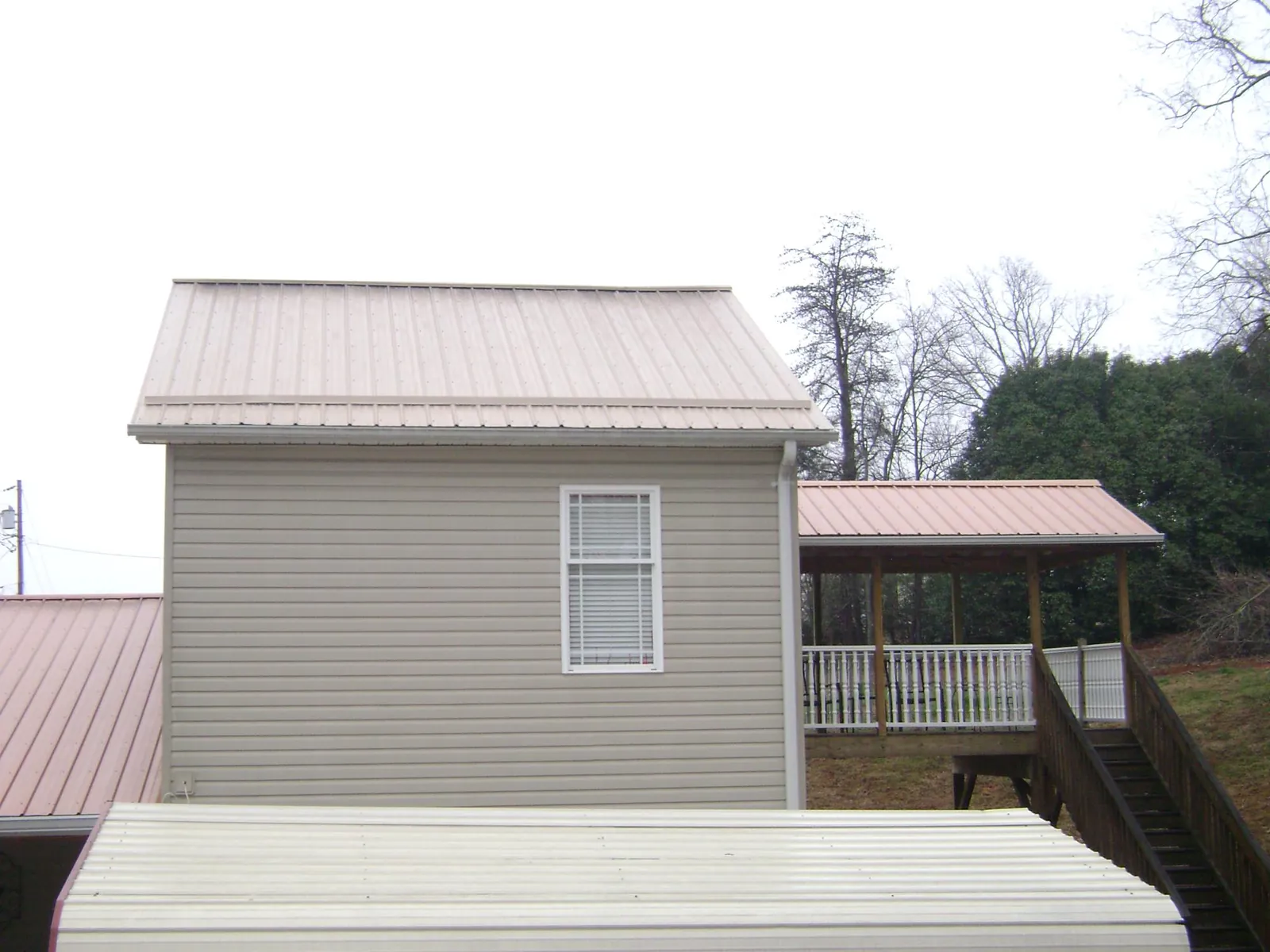 Tan metal roofs on a two story addition and attached porch, from a Roof Replacement job in Ottumwa